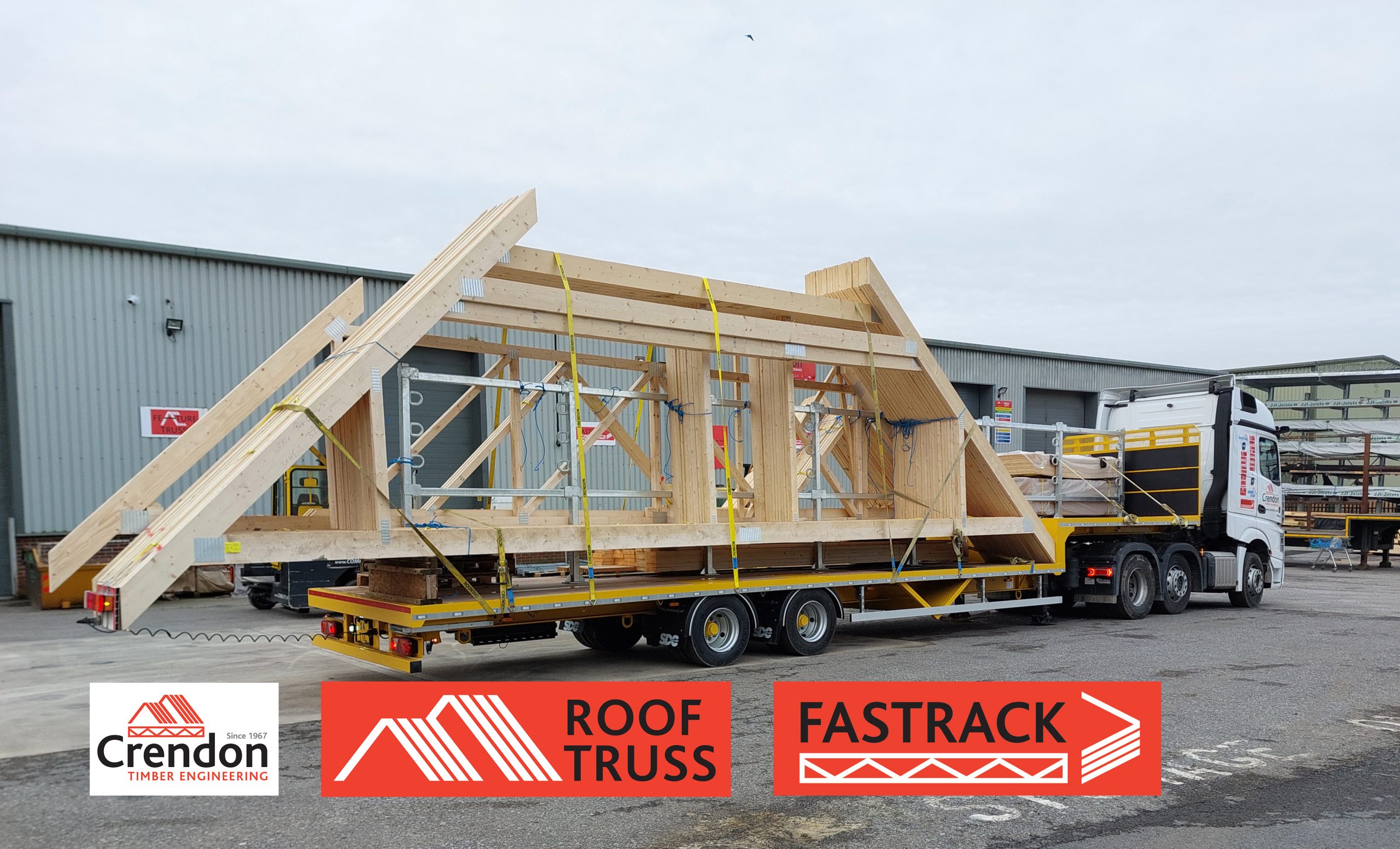 White lorry with yellow trailer loaded with Roof Trusses outside a warehouse with racks of materials