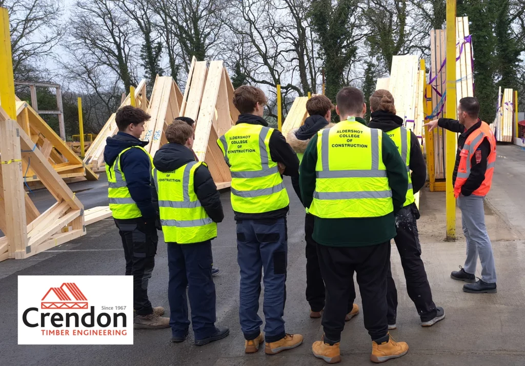 Group of young people in high vis vests being shown around a timber yard looking at roof trusses