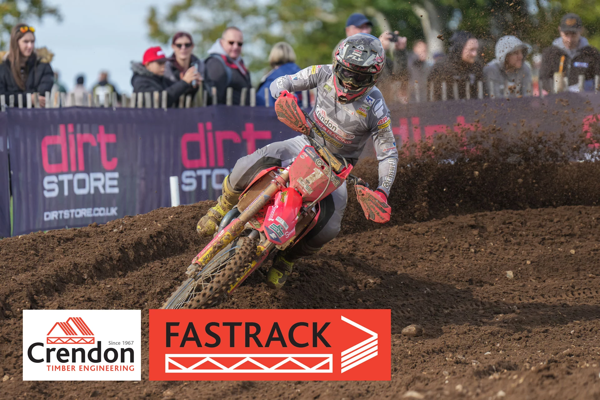 A motocross rider on a dirt track, from the side with mud flying up from the track.