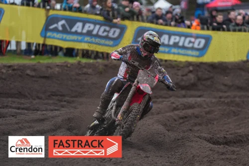 Motocross biker on a dirt track with spectators in the background.