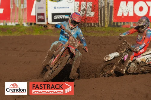 Biker in blue on a red bike on a dirt track with dirt sprayed in the air.