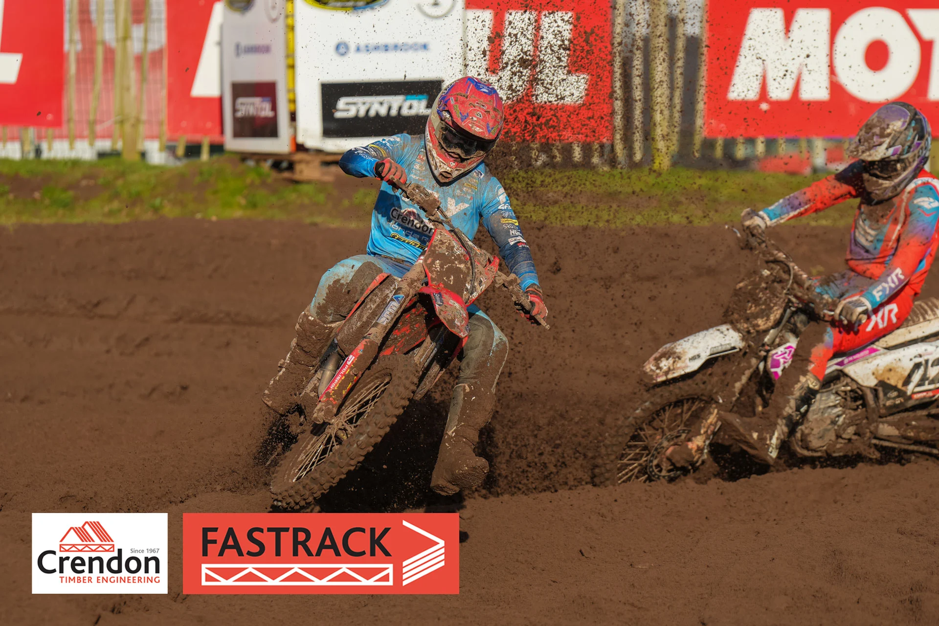 Biker in blue on a red bike on a dirt track with dirt sprayed in the air. 