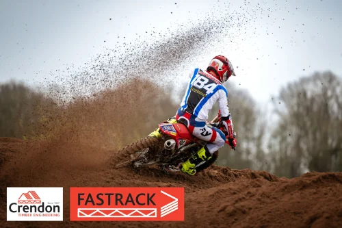 A motocross rider going round the bend with mud flying off the back wheel. 
