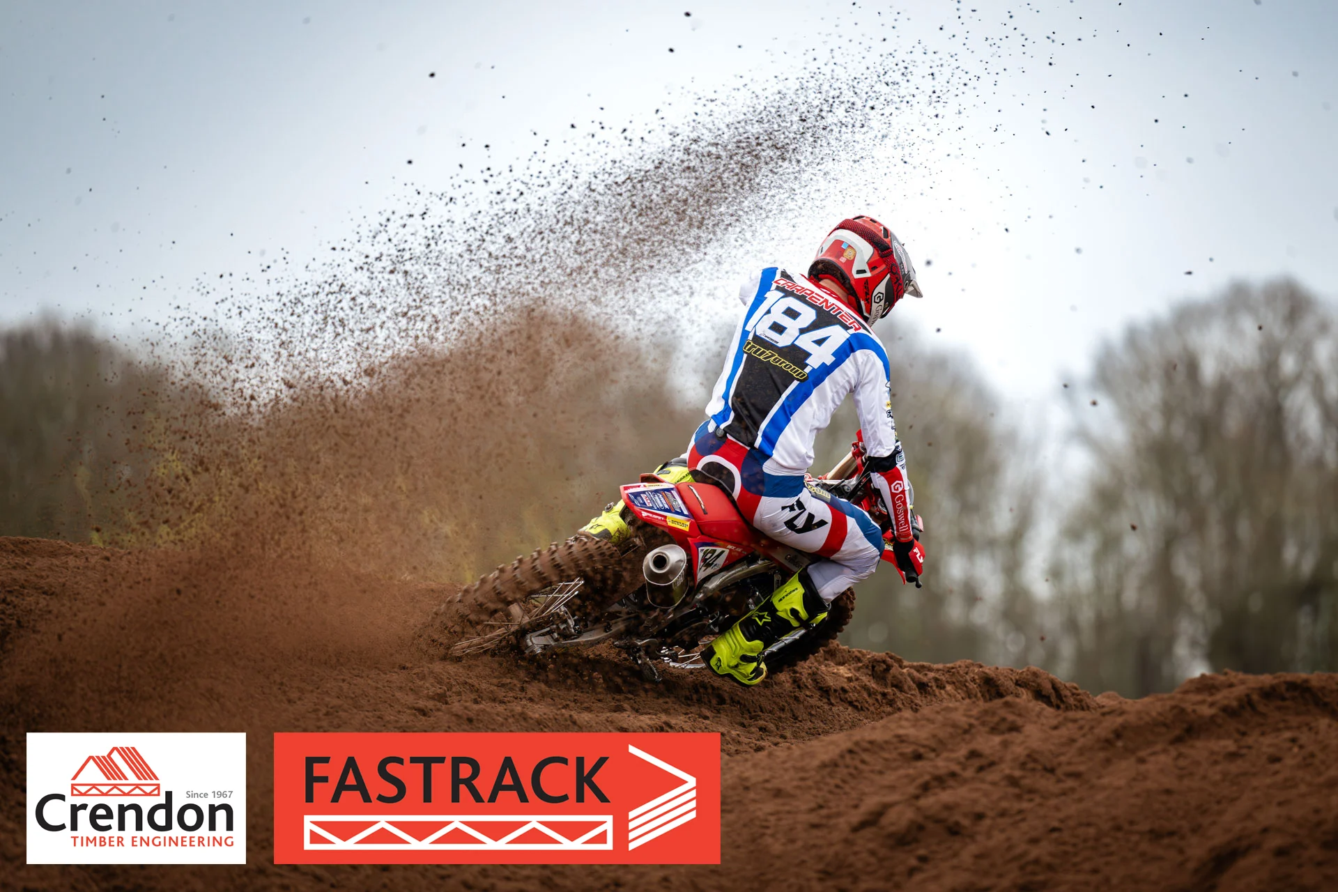 A motocross rider going round the bend with mud flying off the back wheel. 