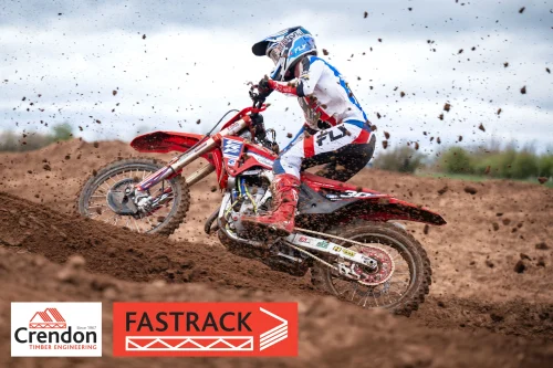 A motocross rider on a dirt track,  from the side with mud flying up from the track.