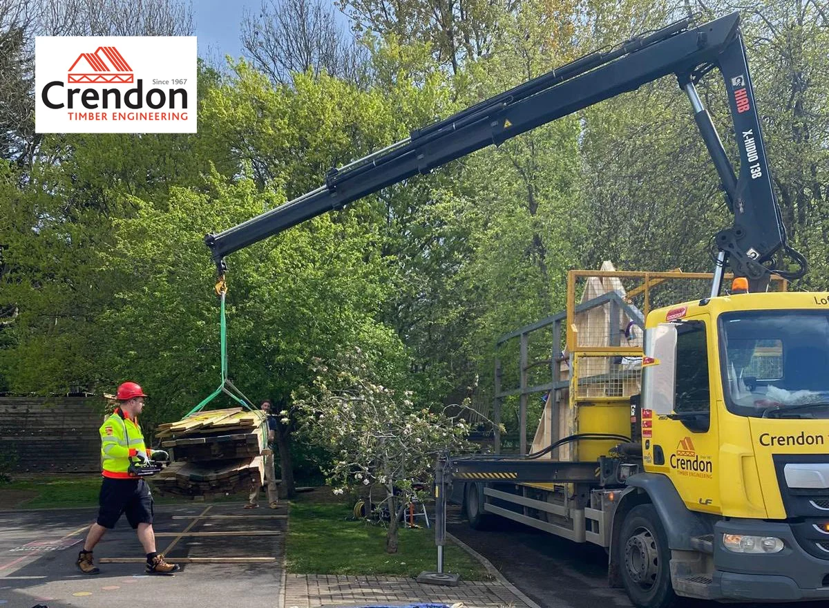 Crendon Crane lifting wooden materials down to the ground in a car park surrounded by trees.