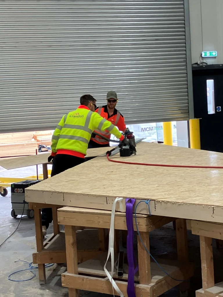 Two workers working with timber materials on a work bench