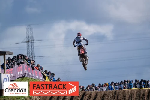 A motocross rider up in the air with a crowd in front of them watching.