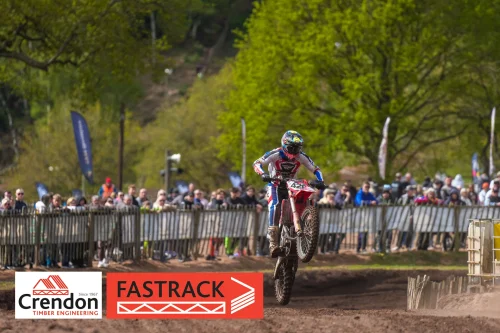 One of the bikers doing a wheelie in front of the crowd on the course.